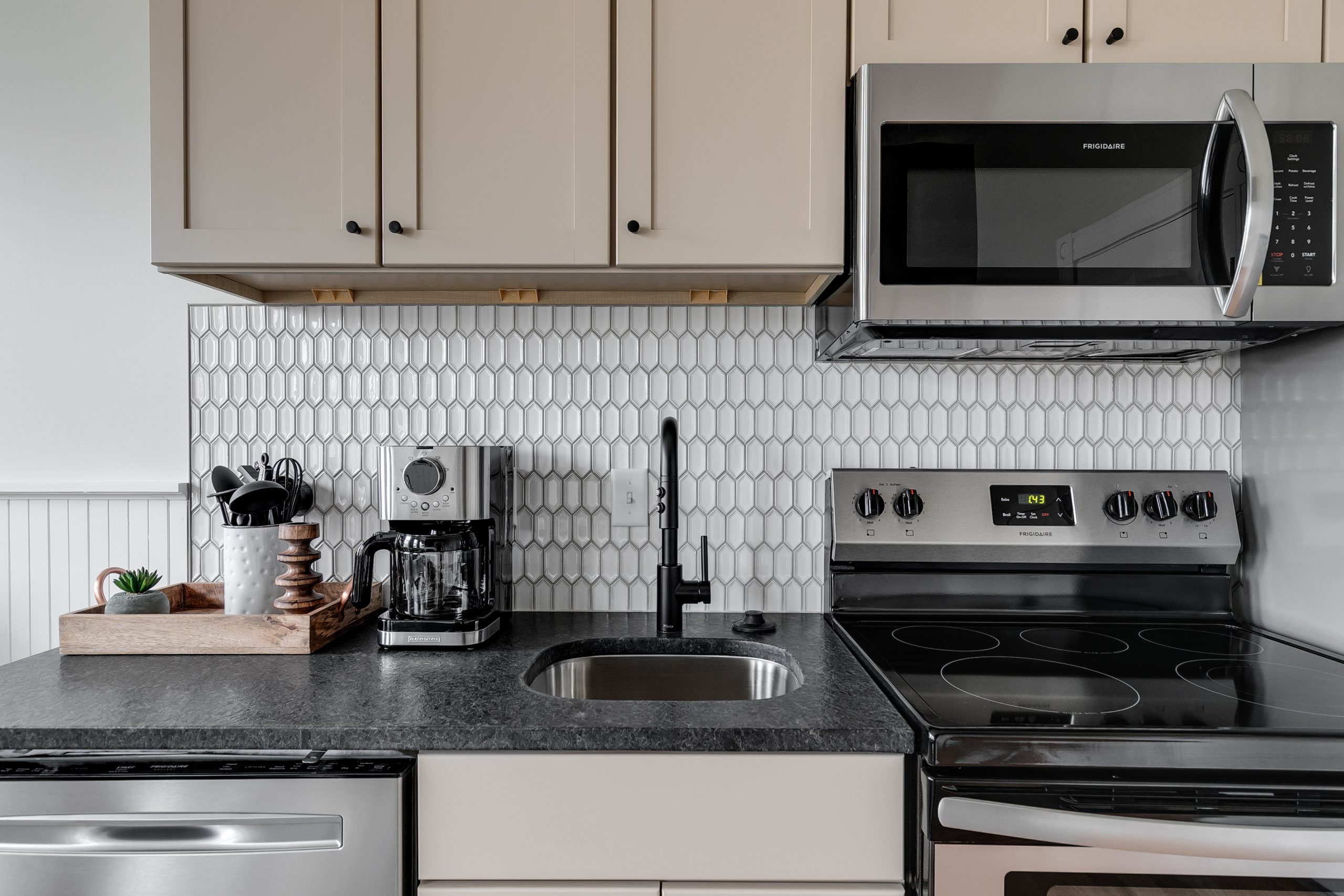 A stylish fully-equipped kitchen with brushed black hardware, cream cabinets, silver appliances, and a white backsplash tiling