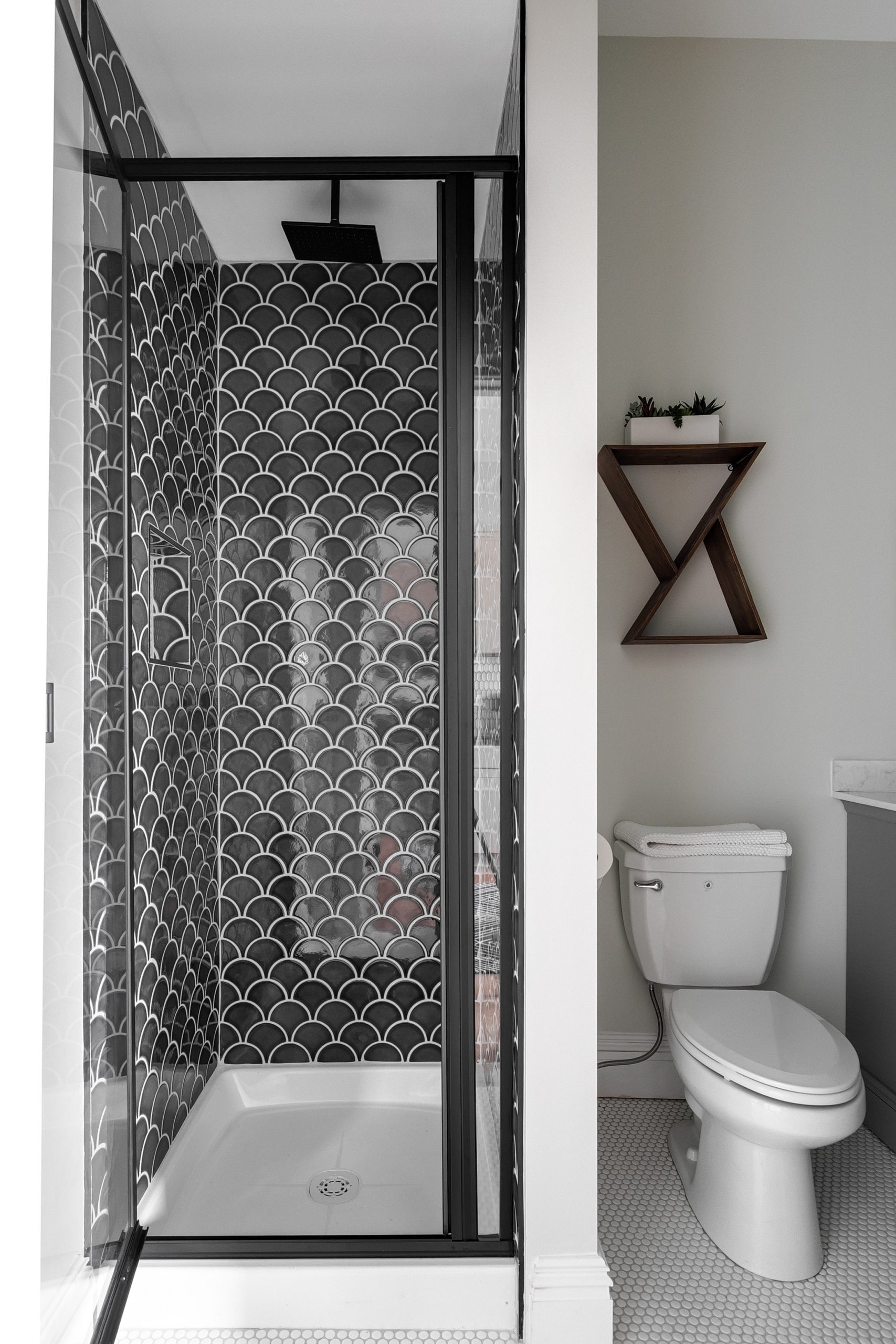 A modern shower surrounded by black "fish scale" tiling on the walls and a brushed black rainfall shower head