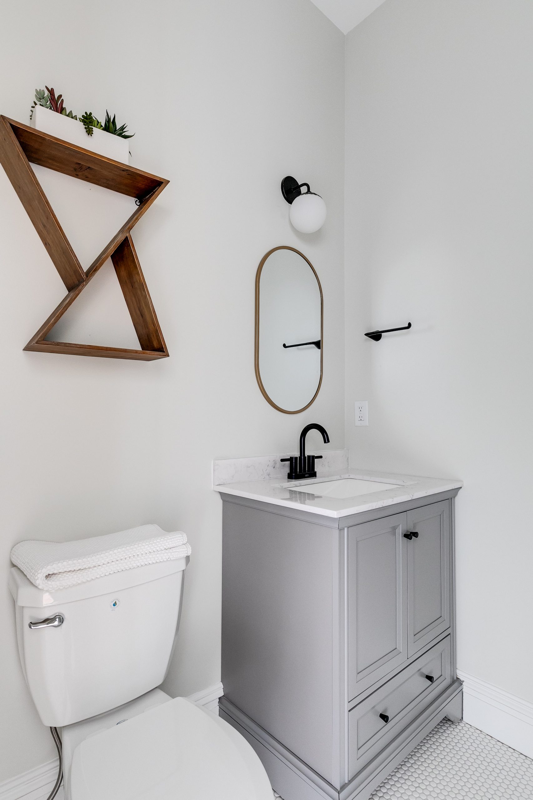 A modern white bathroom with a grey vessel sink furnished with black metal hardware.