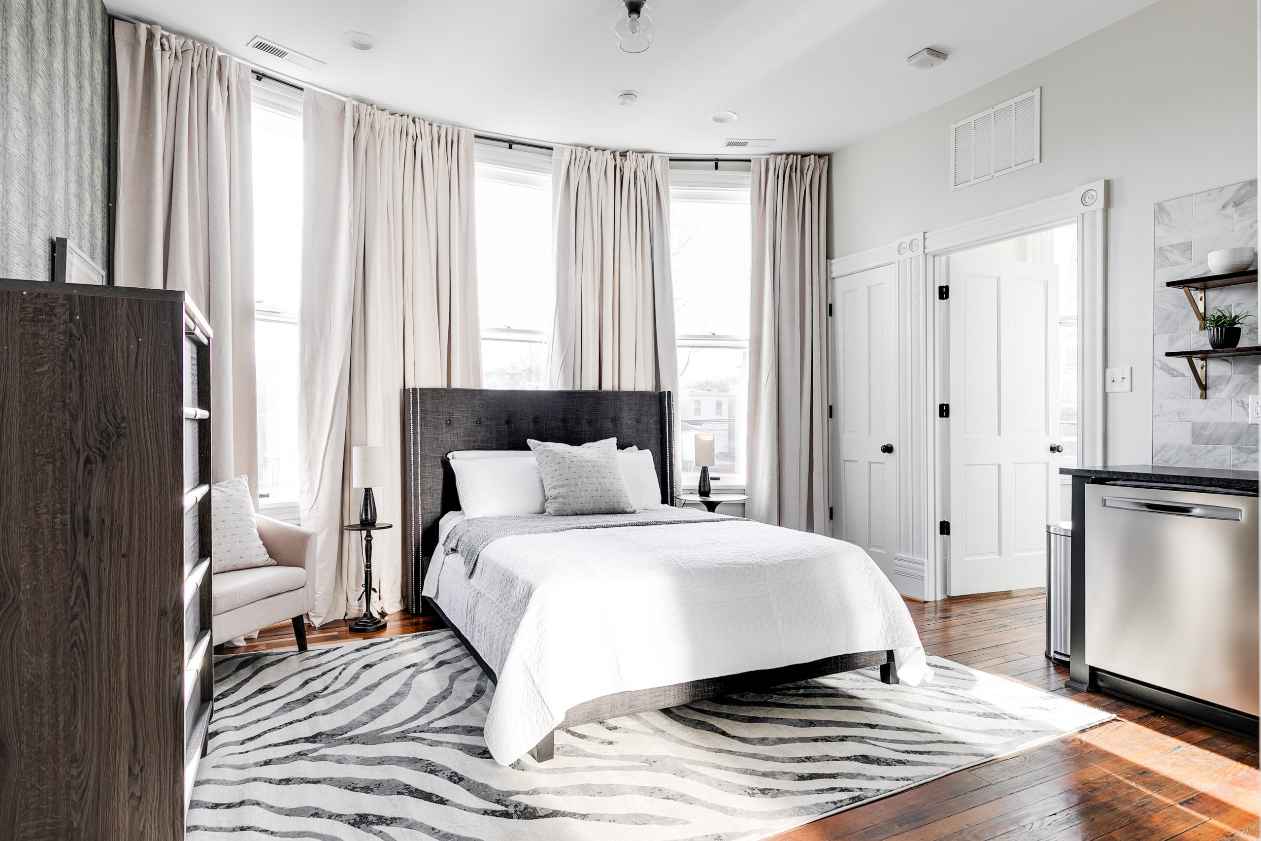 A modern white/cream bedroom with large bay windows and grey accents throughout.